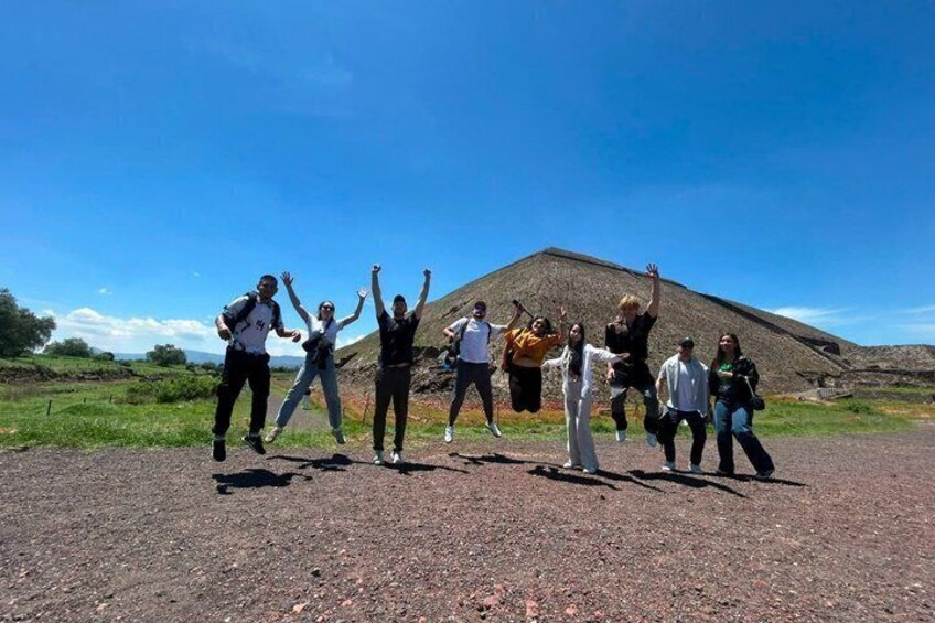 A group of people dancing on a dirt road with a large mound in the background. 5