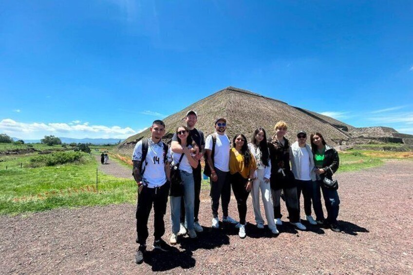 A group of people standing in front of a large pyramid-like structure in a clear, open field. 3