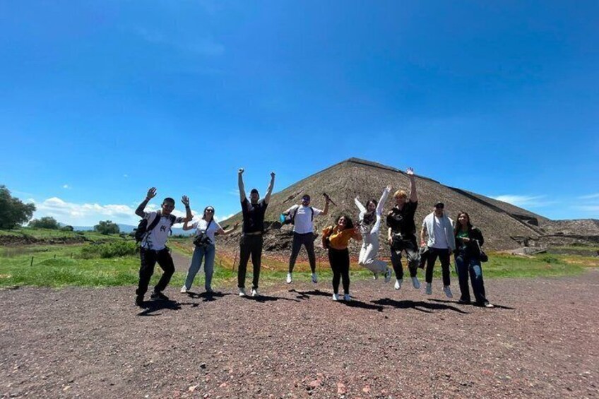 A group of people standing on a dirt road with a large pyramid-like structure in the background. 2