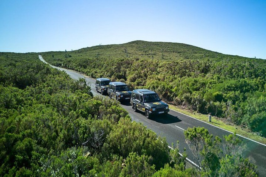A convoy of vehicles on a winding road through a hilly, green landscape. 1