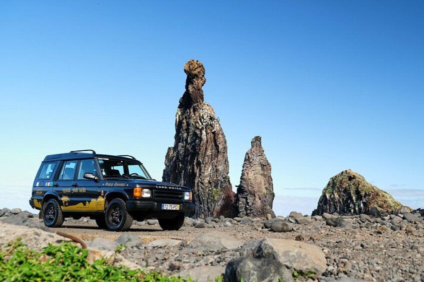 A blue SUV parked on rocky terrain with a prominent rock formation in the background. 2