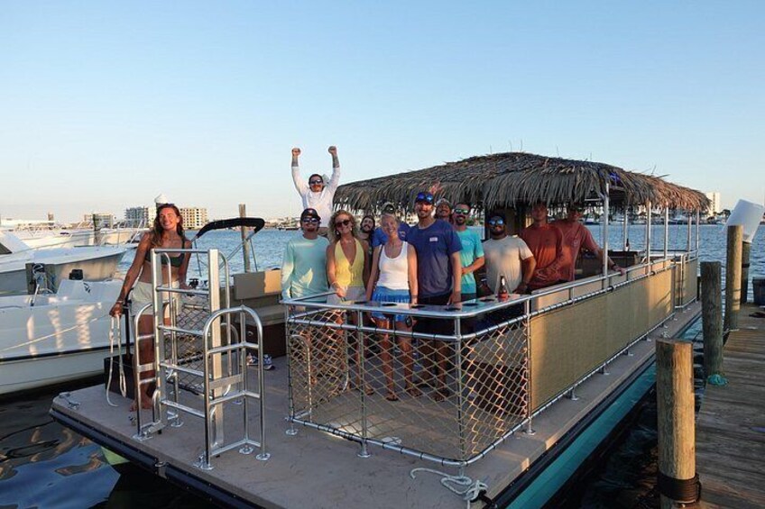 Un grupo de personas en un bote amarrado en un puerto deportivo con una estructura de techo de paja. 3