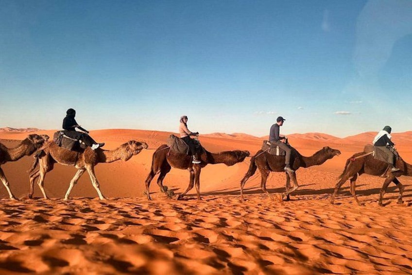 A group of people riding camels across a desert landscape. 1