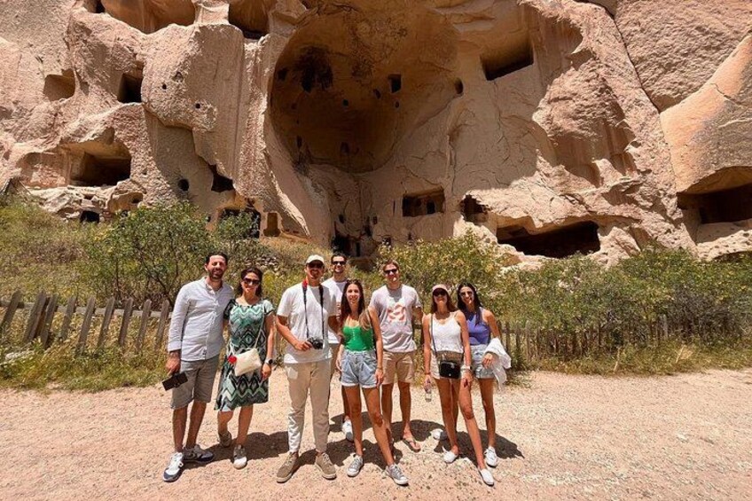 A group of people standing in front of a large rock formation with multiple caves. 3