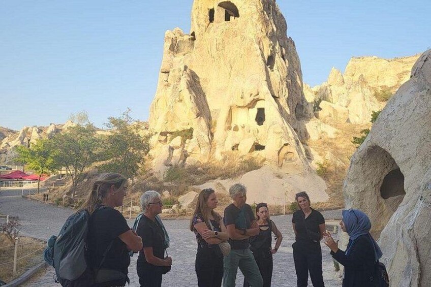 A group of people standing in front of a large rock formation with multiple caves. 5