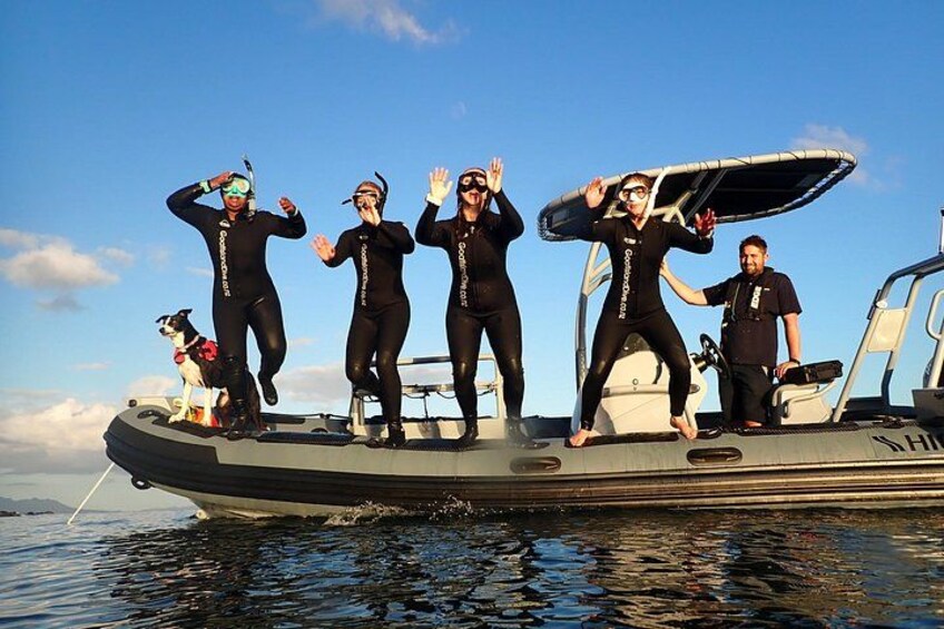A group of people in wetsuits on a boat with a dog. 4