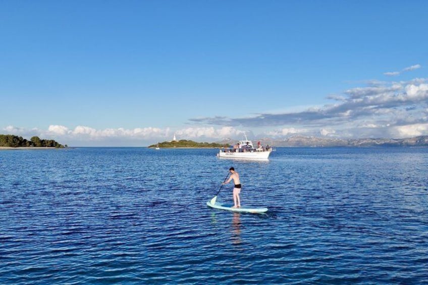 A person paddleboarding on calm waters with a boat in the background. 2