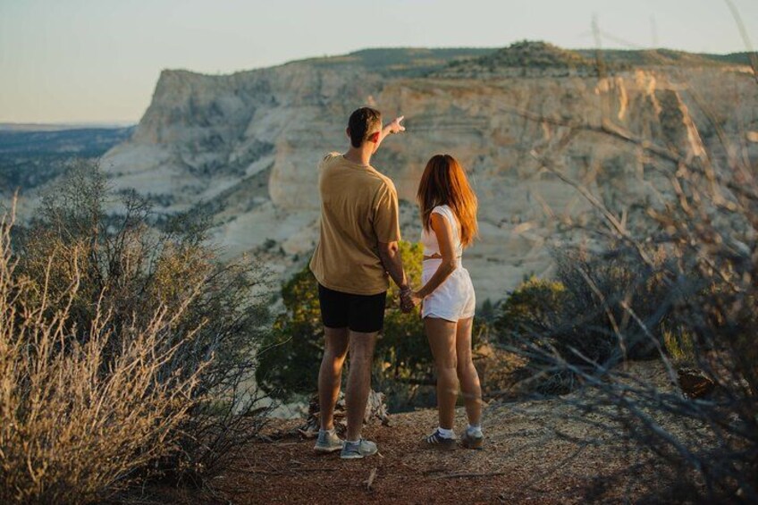 Two people standing on a rocky outcrop overlooking a canyon with sparse vegetation. 2