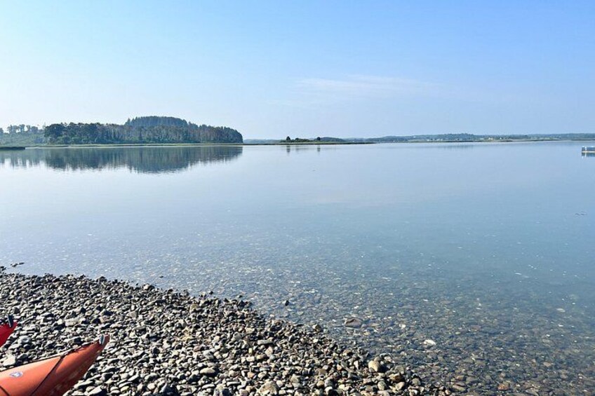 A calm lake with a rocky shoreline, a small island in the distance, and a clear sky. 4