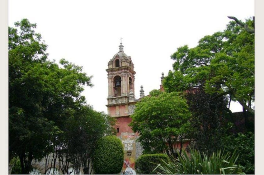 A historic church with a bell tower, surrounded by lush green trees. 1