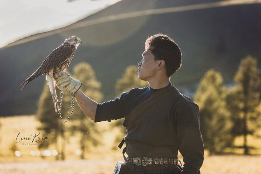 A person holding a bird of prey with a mountainous landscape in the background. 2
