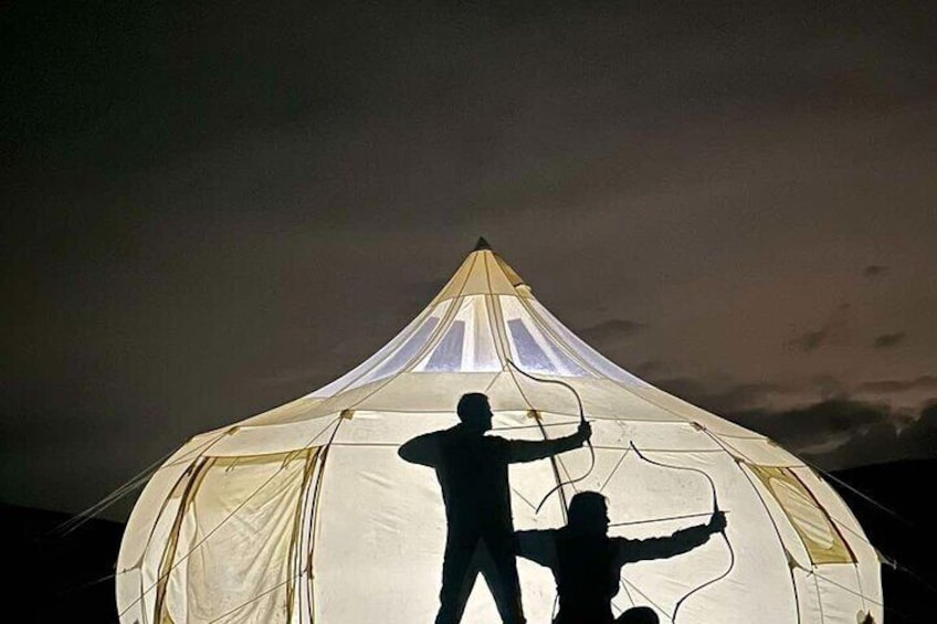 A large tent with two people silhouetted against it, one standing and one sitting. 5