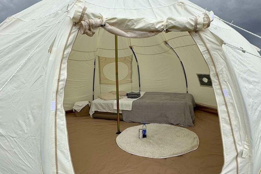 A tent with a bed inside, a small table, and a mat on the floor. 3
