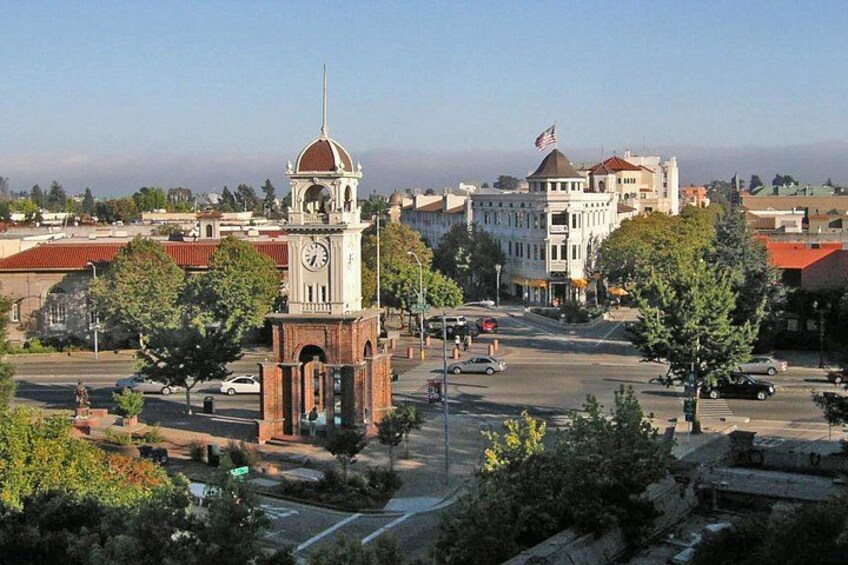 A town square with a clock tower, a large building with a dome, and a statue. 2