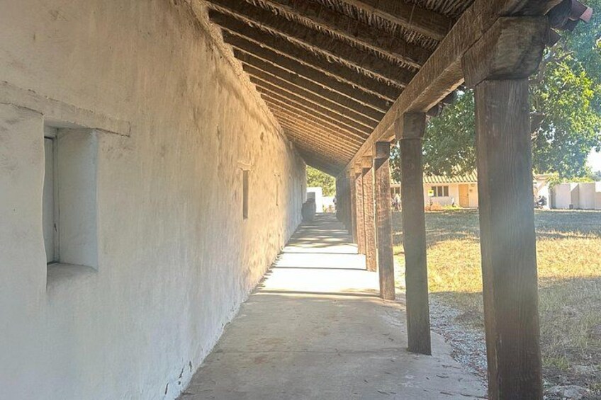 A covered walkway with wooden beams and columns, leading to a building with a white wall. 3