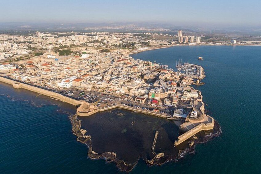 An aerial view of a coastal city with a fortified harbor, dense urban area, and a clear blue sea. 4