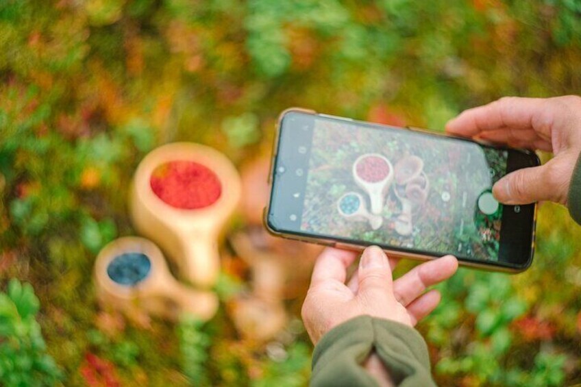 A person holding a smartphone, taking a photo of wooden containers with colorful contents. 5