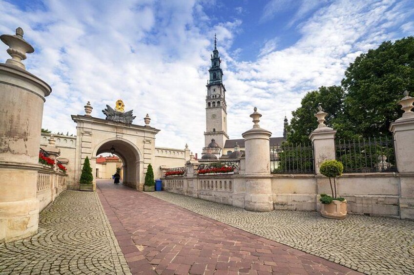 A cobblestone pathway leading to a historic archway with a tower in the background. 5