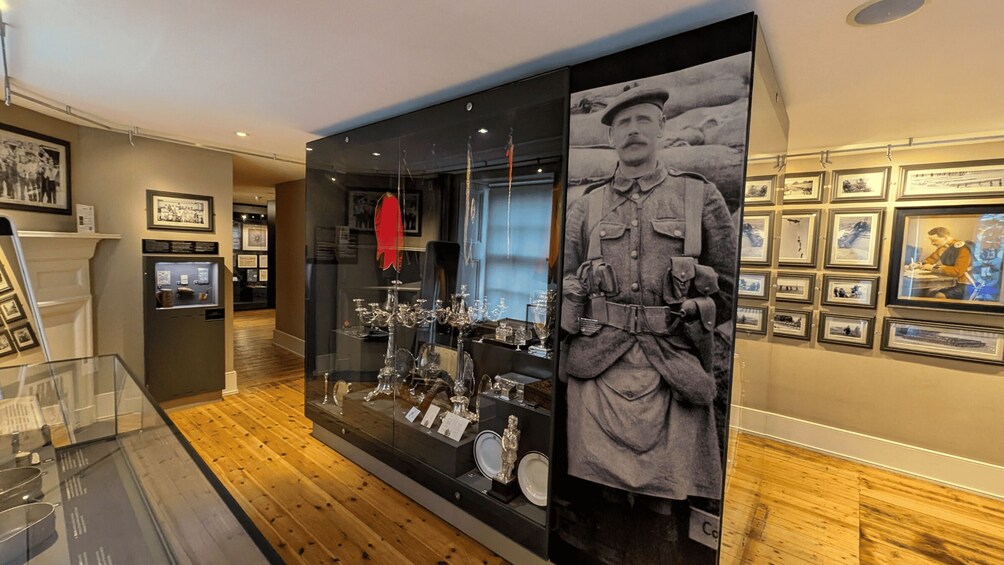 A museum exhibit with a glass display case containing silverware and a large photograph of a soldier. 2