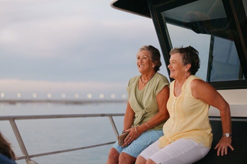 Two people sitting on a boat with a body of water and a bridge in the background. 5