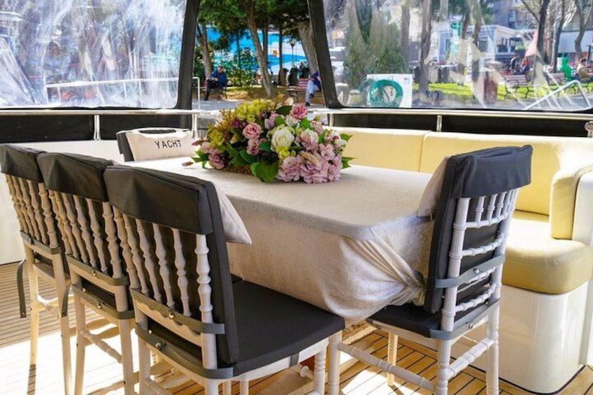 Un espace repas sur un yacht, comprenant une table, des chaises et un arrangement floral en guise de décoration centrale. 2
