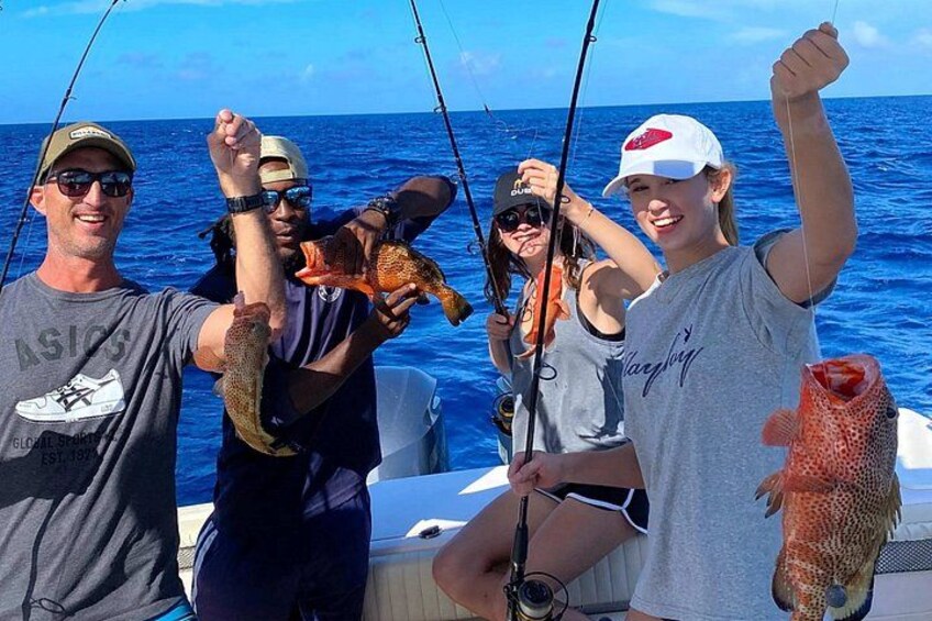 Cuatro personas en un bote sosteniendo peces, con el océano al fondo. 1