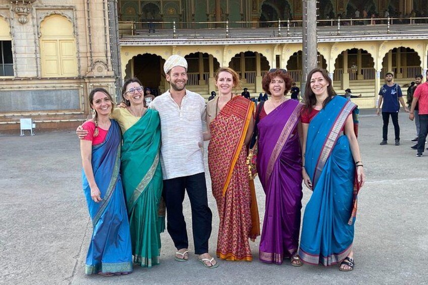 A group of people in traditional attire posing in front of a historic building with arches and detailed architecture. 2