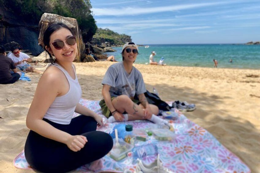 Une plage où des personnes sont assises sur une couverture, avec une falaise rocheuse en arrière-plan et la mer. 1