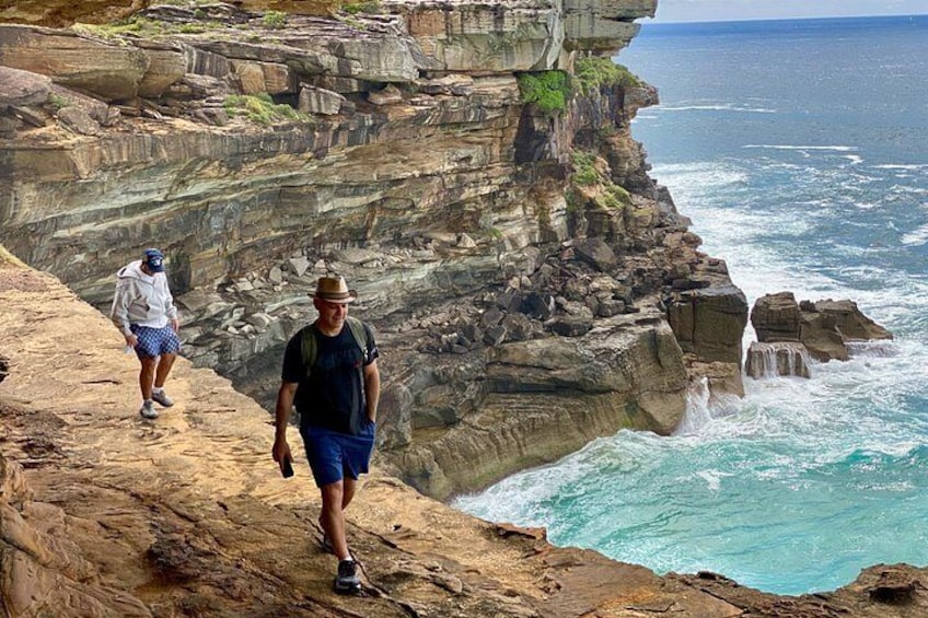 Due persone camminano su una scogliera rocciosa vicino all'acqua. 1
