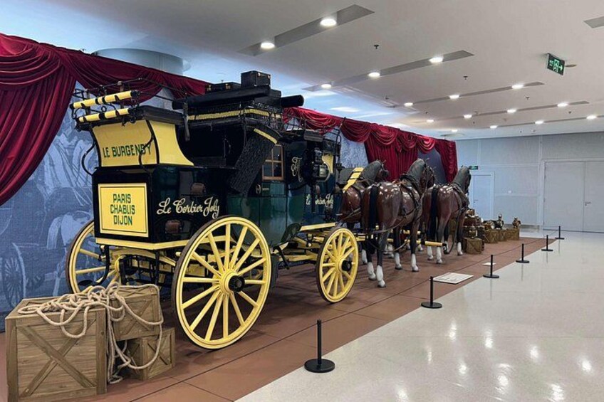 A vintage Parisian carriage with horses, displayed indoors with red curtains and a polished floor. 3