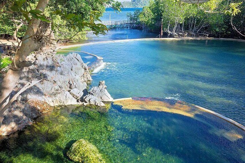 A clear blue water body surrounded by rocky terrain and trees. 2