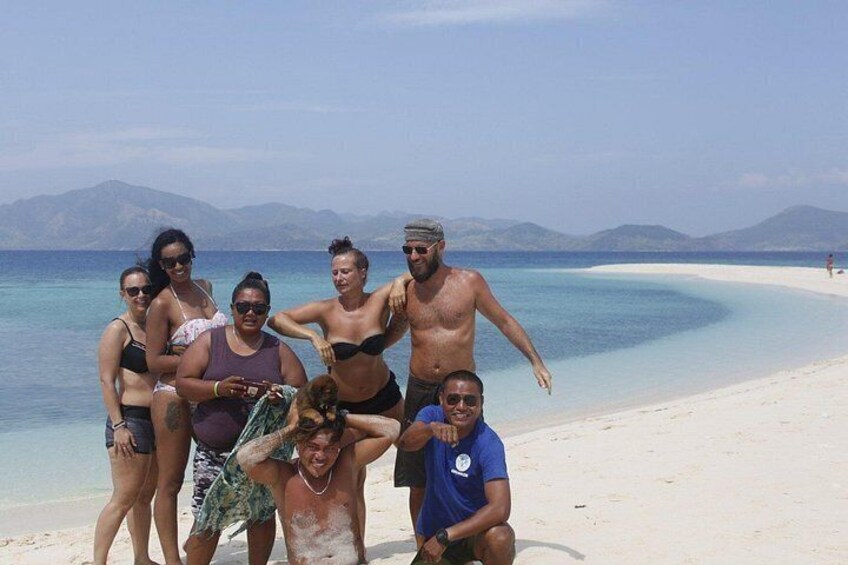 A group of people on a beach with clear blue water and distant mountains. 3