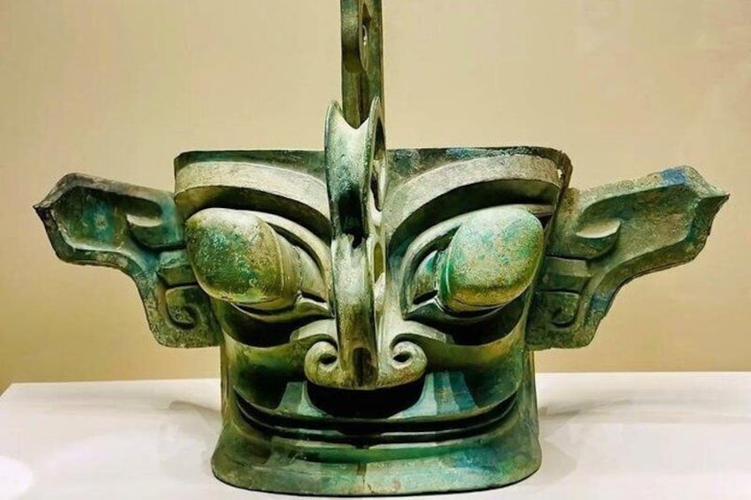 A bronze sculpture with a central face and two wings. 4