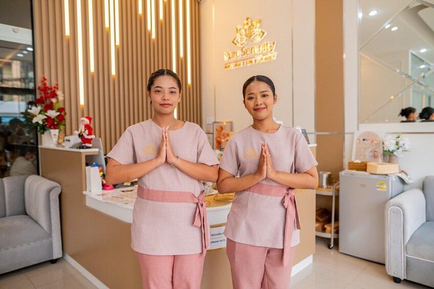Two individuals in a spa-like setting with a reception desk, a mirror, and a decorative wall. 2