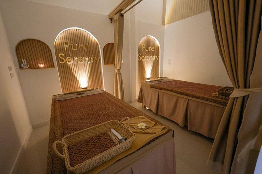 A spa room with two beds, each with a 'Pure Serenity' sign, and a small shelf with a candle. 1