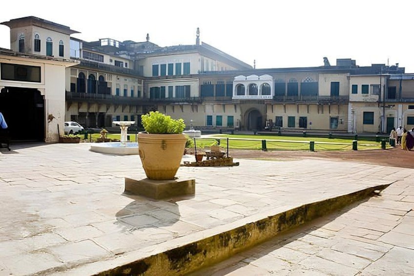 A courtyard with a large planter, a fountain, and historic buildings in the background. 4