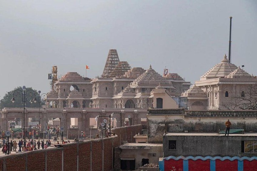 A historical building with multiple domes and arches, surrounded by a low wall and a few people. 1