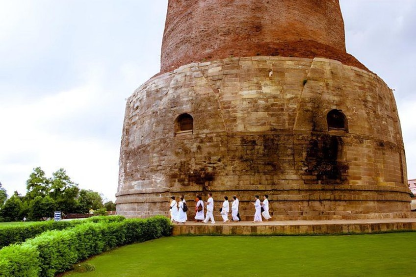A large, cylindrical stone structure with a red top, surrounded by a well-maintained lawn and a few people in white clothing. 2