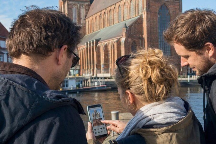 Tres personas mirando un teléfono inteligente, con un edificio histórico y un río al fondo. 5