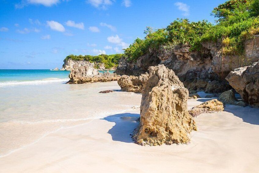 A sandy beach with clear turquoise water, rocky formations, and green vegetation. 4