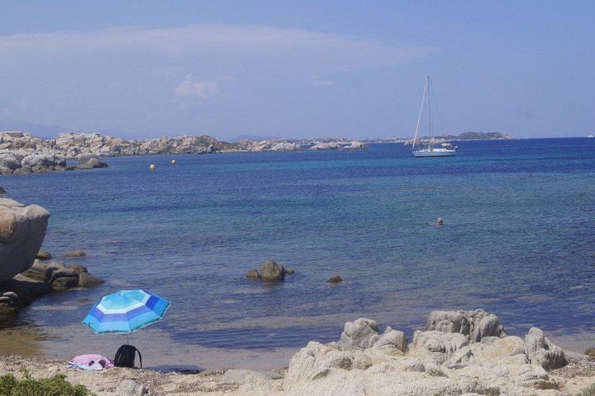A beach with rocks, a sailboat, and a person swimming. 5