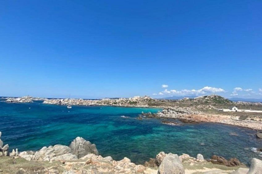 A coastal landscape with clear blue waters, rocky outcrops, and a distant shoreline. 1