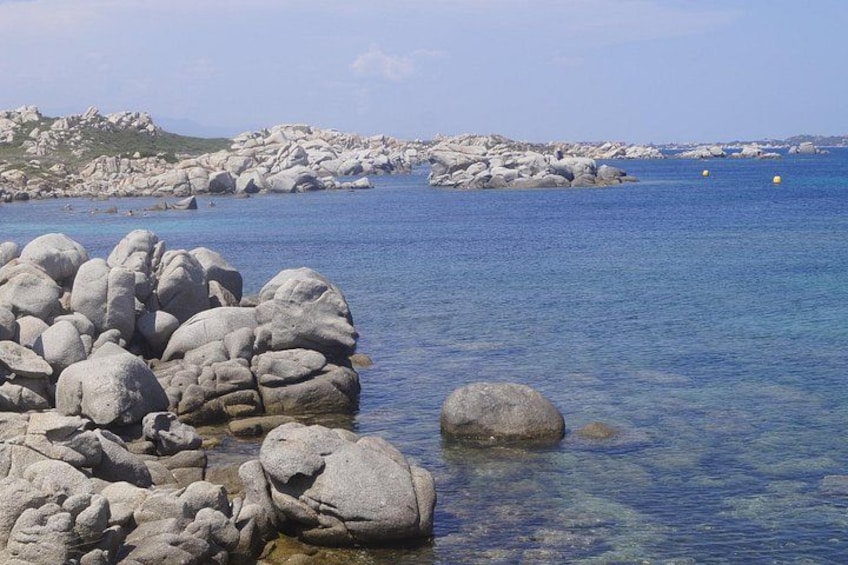 A rocky shoreline with clear blue water and distant land. 4