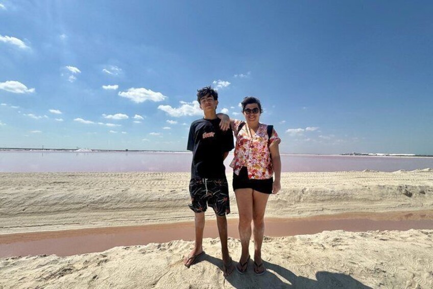Dos personas de pie en una playa arenosa con una masa de agua rosada al fondo. 4