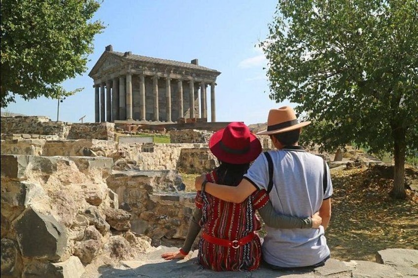 A couple sitting on a stone platform overlooking ancient ruins with columns and a temple-like structure in the background. 4