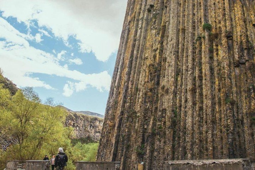 A large rock formation with vertical striations, surrounded by greenery and a clear sky. 5