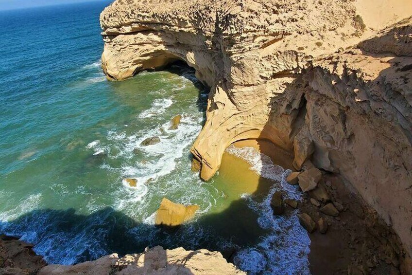 A coastal cliff with a cave-like formation and a small pool of water at its base. 1