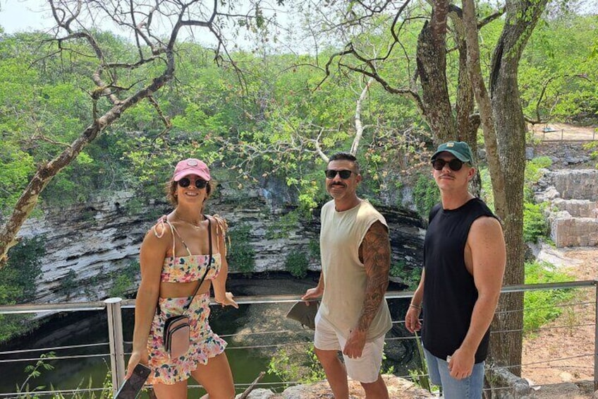 Three people standing by a water body with trees and rocky terrain in the background. 2