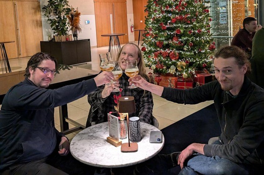 Tres personas brindando con copas en una mesa redonda, con un árbol de Navidad al fondo. 3