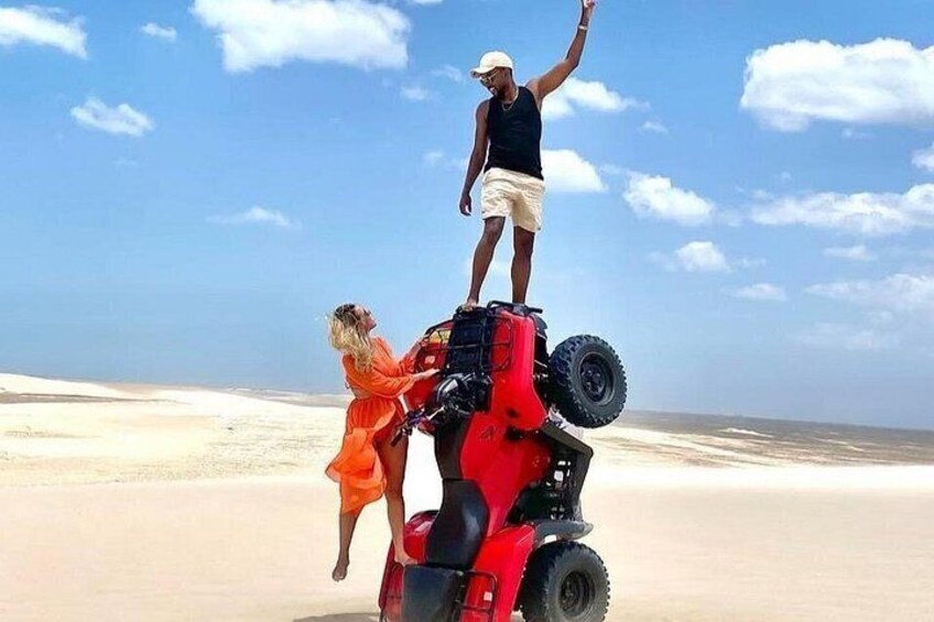 A person standing on a red vehicle on a beach with sand dunes in the background. 3